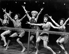 four women in bathing suits are dancing on the stage with their hands up and one woman has her arms raised