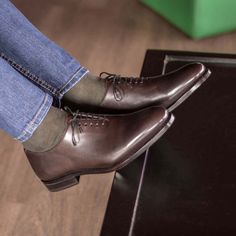 a person sitting on top of a wooden table wearing brown dress shoes and blue jeans