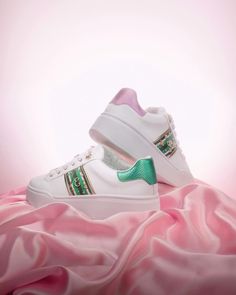 a pair of white sneakers with green and pink trims on top of a pink blanket