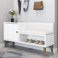 a white bench sitting under a coat rack next to a vase with flowers on it