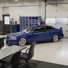 a blue car parked in a garage next to a table and chairs on the floor