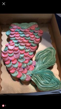 a decorated cake in the shape of a mermaid tail with pink, green and blue icing