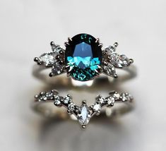 a blue diamond ring sitting on top of a white table next to a pair of diamonds