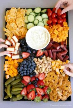 two hands reaching for fruit and crackers on a tray