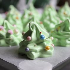 some green frosted christmas trees are on a tray with other cookies in the background