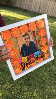 a person holding up a framed photo with orange flowers on the grass in front of them