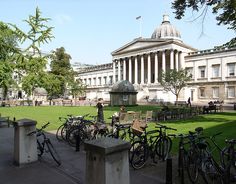 people sitting on benches in front of a large building with a clock tower and green grass