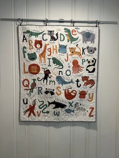 a quilt hanging on the wall with letters and animals