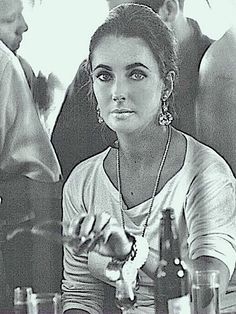 a black and white photo of a woman sitting at a table with beer bottles in front of her