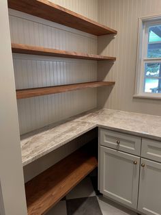 an empty kitchen with white cabinets and wood shelves