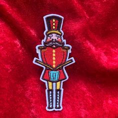 a red velvet background with an embroidered patch depicting a nutcracker