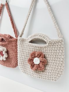 two crocheted purses hanging on the wall with flowers attached to them, one in pink and one in white