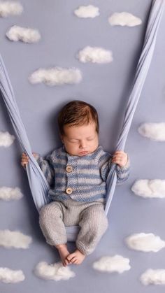 a baby is laying in a hammock with clouds on the wall behind him