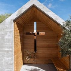 the inside of a wooden church with a cross on it's wall and an olive tree in front