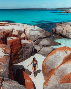 a woman in a bathing suit walking on the beach next to some rocks and water