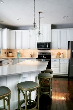 a kitchen with white cabinets and an island in the middle is lit by pendant lights