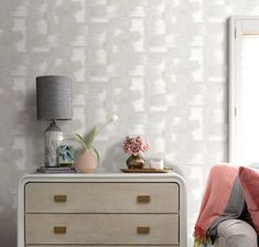 a bedroom with a dresser, lamp and flowers on the side table in front of it