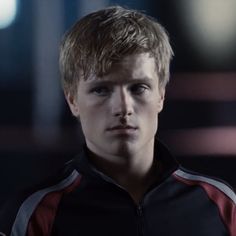 a young man with blonde hair wearing a black and red jacket looking at the camera