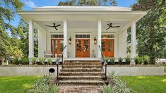 a white house with red doors and steps leading up to the front door is surrounded by greenery