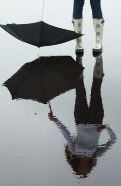 a person standing in the rain with an umbrella over their head and reflection on the wet ground