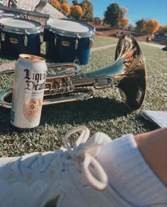 a can of beer sitting on top of a field next to a trumpet and some drums