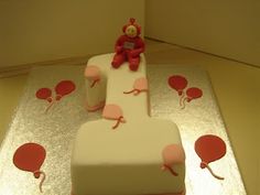 a birthday cake decorated with balloons and a teddy bear on the top one is red