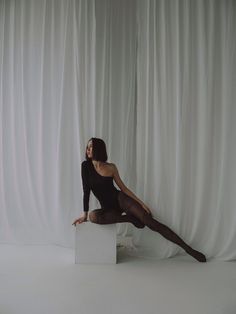 a woman sitting on top of a white block in front of a white curtain wearing black stockings