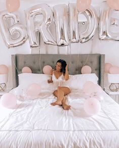 a woman sitting on top of a bed in front of balloons and letters that spell out the word bridal