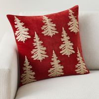 a red and white pillow with gold trees on it sitting on a couch in front of a white chair