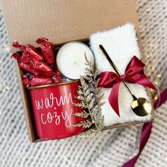 a box filled with candles and other holiday items next to a red mug that says warm cosy