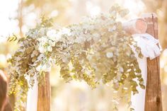 the bride and groom are getting married under an arch decorated with greenery for their wedding ceremony