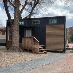 a tiny house with stairs leading up to the front door and side porch, next to a tree