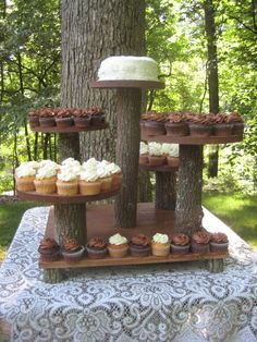 cupcakes are arranged on three tiered trays in front of a tree