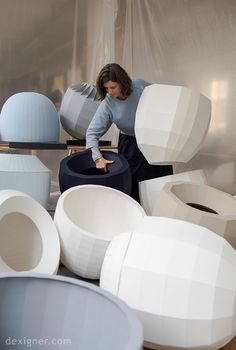 a woman standing in front of several large white vases on top of a table