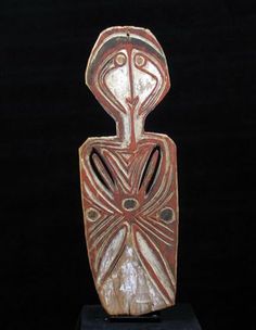 an old wooden statue with designs on it's face and body, sitting on a black surface