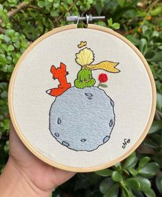 someone is holding up a small embroidery project with an image of the little prince on it