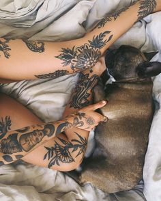 a woman laying in bed with tattoos on her arms and legs next to a dog