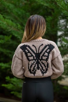 the back of a woman's sweater that has a butterfly on it and is in front of some trees