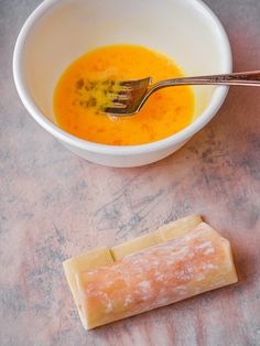 a bowl of soup next to a piece of butter and a spoon on a table