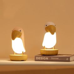 two small wooden birds sitting on top of a table next to a book and lamp