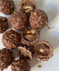 chocolate covered donuts on a white plate with nuts in the middle and one bite taken out