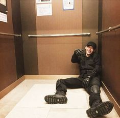 a man sitting on the floor in an elevator with his feet propped up and wearing skis