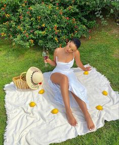 a woman sitting on top of a blanket holding a glass of wine and lemons