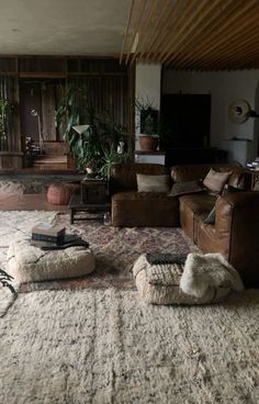 Immerse yourself in the ultimate cozy retreat, where comfort meets rustic elegance 🌿🛋️. This inviting space features ultra-soft sheepskin poufs, a classic brown leather couch, and plush rugs that make every step feel like a walk on clouds. Surrounded by wood-paneled walls that exude warmth and charm, and accented with an abundance of lush green plants, this living area is a sanctuary of relaxation and style. Perfect for those who love to blend luxurious textures with the natural beauty of the outdoors. #CozyHome #RusticElegance #PlantDecor #HomeStyle #InteriorDesign Earthy Home Design, Cute Farmhouse, Ottoman Pouf, House Room, Room Inspiration Bedroom