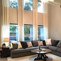 a living room filled with lots of furniture next to two large windows covered in white drapes