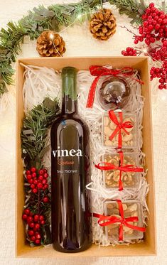 a bottle of wine sitting in a box next to christmas decorations and pineconis