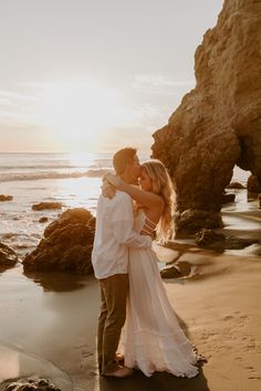 a bride and groom embrace on the beach at sunset