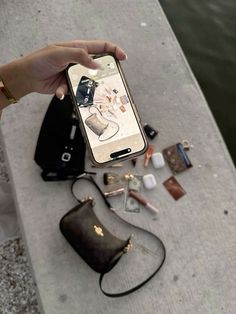 someone is holding their cell phone near the water with other items on it, including an empty purse