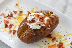 a baked potato with bacon, cheese and sour cream sits on a square white plate