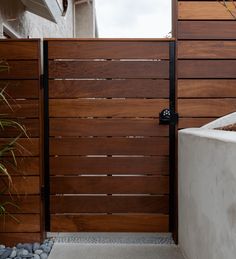 a wooden gate in front of a white house with rocks and plants on the side